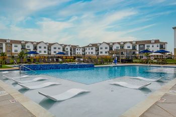 A large swimming pool with a blue tinted water in front of a building with white walls and brown roofs.